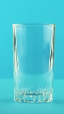 Dikey video 4K yakın plan sarı limonlu limonata, soğuk içecek. Stüdyoda bardaktan yapılmış mavi arka planda duruyor.