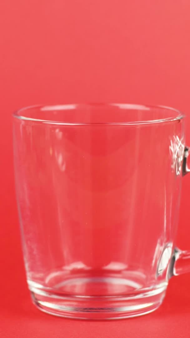 Vertikal video Kaffebönor hälla snabbt, transparent glas kopp, röd bakgrund. Energikoncept — Stockvideo