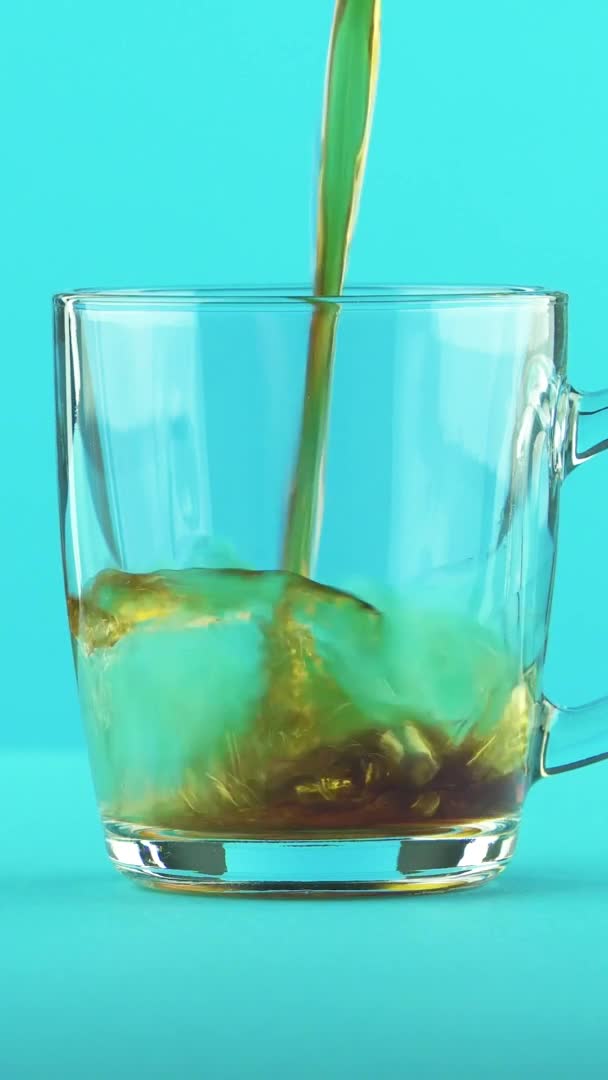 Függőleges videó 4K közelkép szénsavas kóla szóda hideg ital pooring üveg bögre lekerekített fogantyú kék háttér stúdió — Stock videók