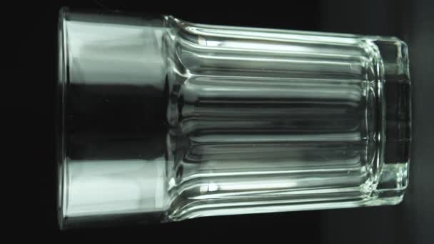 Vertikální video Mléko nalévání do fasetovaného skla zblízka izolované na černém pozadí — Stock video