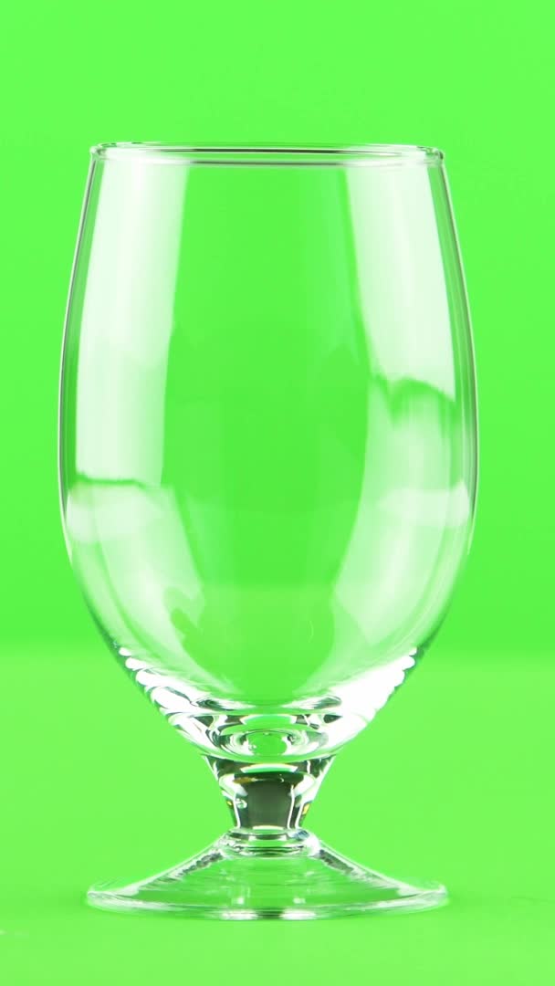 Vertical video Jugo vertiendo en copa aislada sobre fondo verde claro — Vídeos de Stock