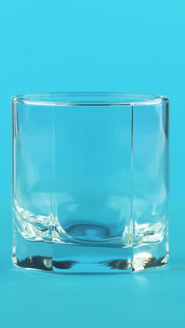 Verticale video 4K close-up shot van melk koude drank arm in laag glas met facetten blauwe achtergrond in de studio — Stockvideo