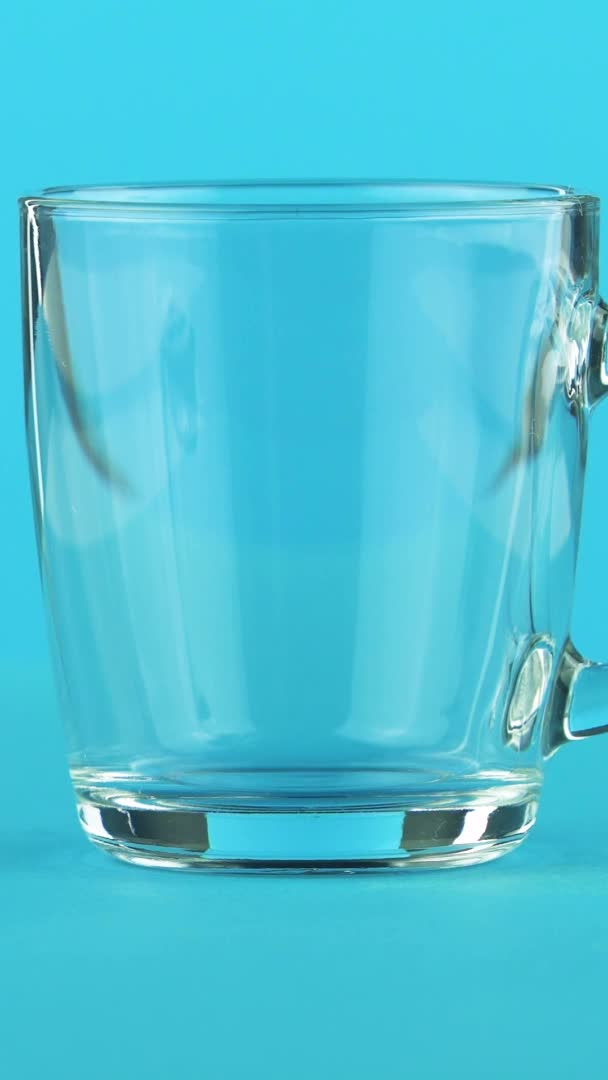 Vertikální video 4K detailní záběr studeného nápoje nápoj nápoj pooring do skleněného hrnku se zaoblenou rukojetí modré pozadí ve studiu — Stock video