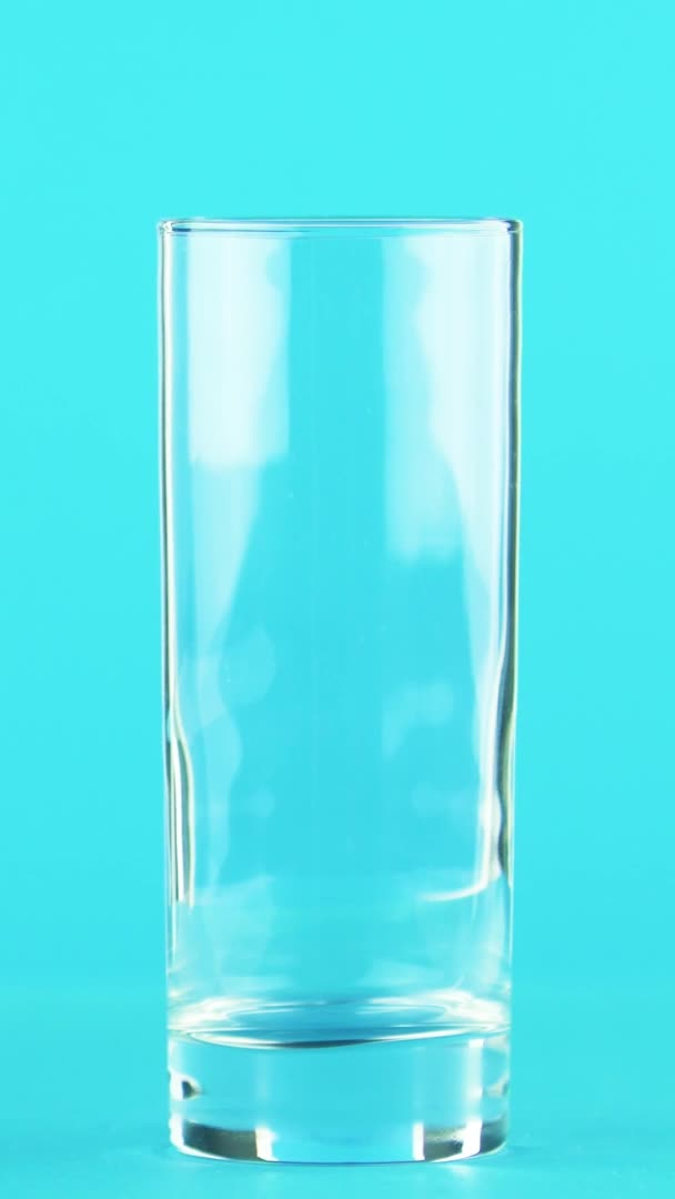 Vertical video 4K close-up shot of fruit orange multifruit juice cold beverage drink pooring into glass blue background in studio — Stock Video