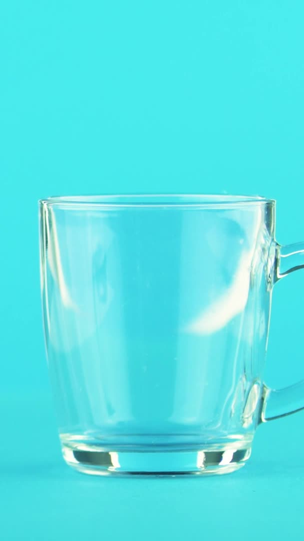 Vertical video 4K close-up shot of fruit orange multifruit juice cold beverage drink pooring into glass mug with rounded handle blue background in studio — Stock Video