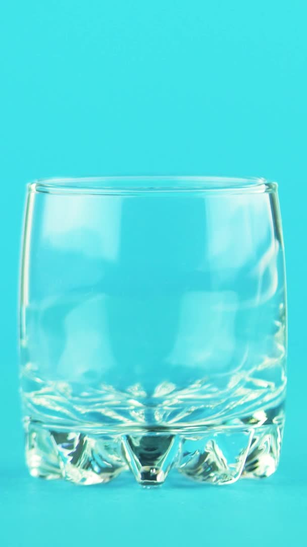 Vertical video 4K close-up shot of milk cold beverage drink pooring into small beautiful glass blue background in studio — Stock Video