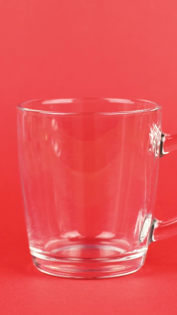 Vertikální video Kávové zrno rychle nalít, transparentní skleněný pohár, červené pozadí. Ranní koncept — Stock video