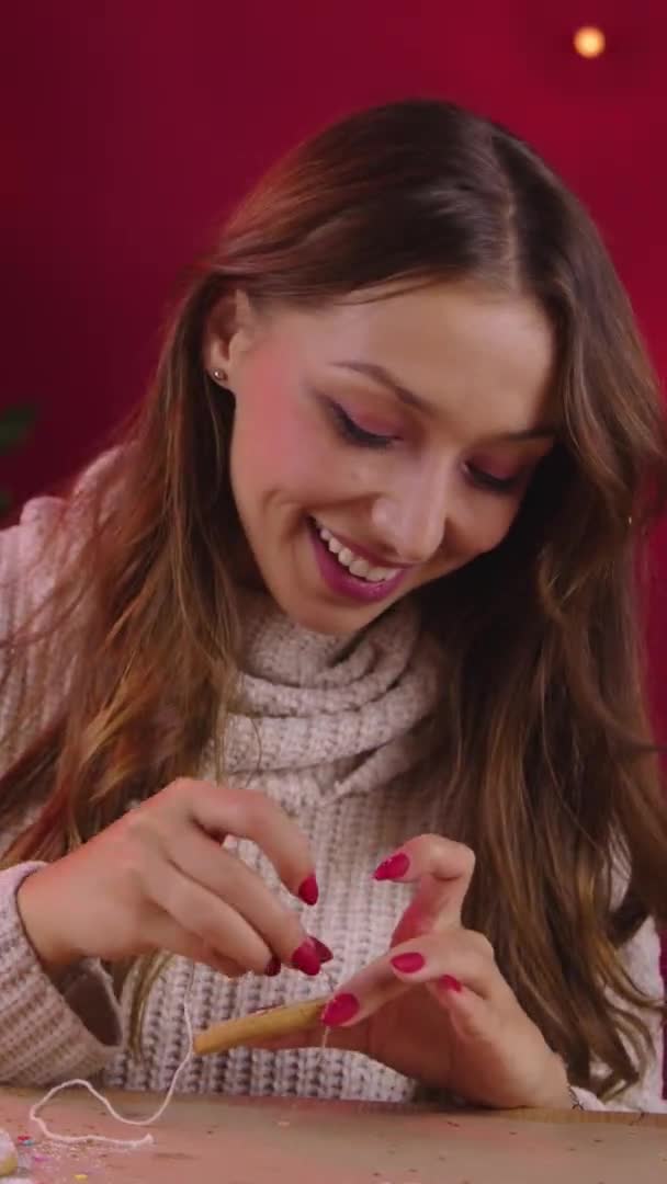 수직 촬영귀엽게 웃는 브루 네트젊은 여자가 아마포줄에 크리스마스 진저브레드를 걸었다 — 비디오