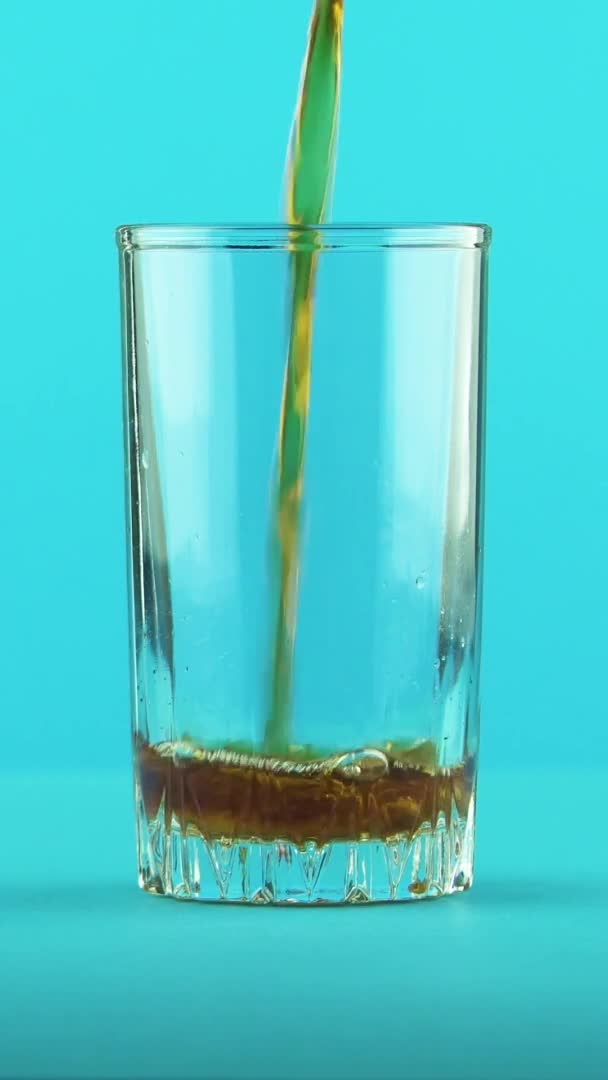Lodret video 4K close-up skud af fizzy cola sodavand kold drik pooring i gevindglas blå baggrund i studiet – Stock-video