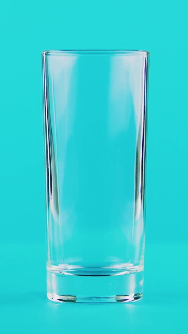 Вертикальное видео 4K крупным планом холодного молочного напитка на низком стеклянном синем фоне в студии — стоковое видео