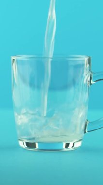 Dikey video 4K yakın çekim sarı limonlu limonata sodası soğuk içecek cam bardağa doluşmuş stüdyoda yuvarlak saplı mavi arka plan