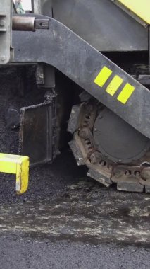 Dikey video Paver yolda asfalt uyguluyor. Kocaman bir ağır ekipman düz sıcak asfalt.