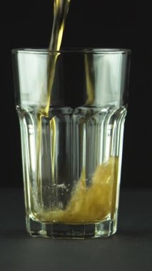 Dikey video Kola, siyah arkaplanda izole edilmiş kabarcıklar ve köpüklerle dolu bir bardağa dökülür.