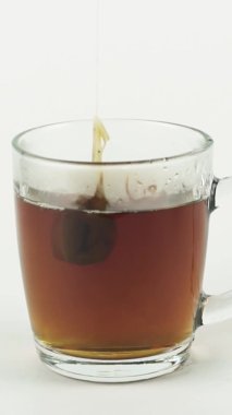 Dikey siyah çay poşeti beyaz arka planda izole edilmiş çayı demlemek için cam şeffaf bardağa yükseliyor ve düşüyor.