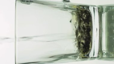 Dikey siyah çay parçacıkları cam şeffaf fincana dökülüyor ve beyaz arka planda izole edilmiş çay demlemek için kaynar suyla dolduruluyor.