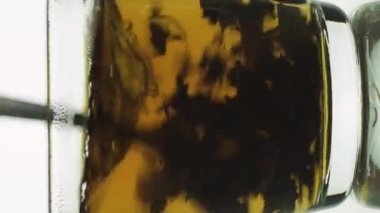 Dikey video kaşığı, şeffaf cam bardakta çay karıştırarak dönen siyah parçacıklar oluşturur. Beyaz arkaplanda izole edildi