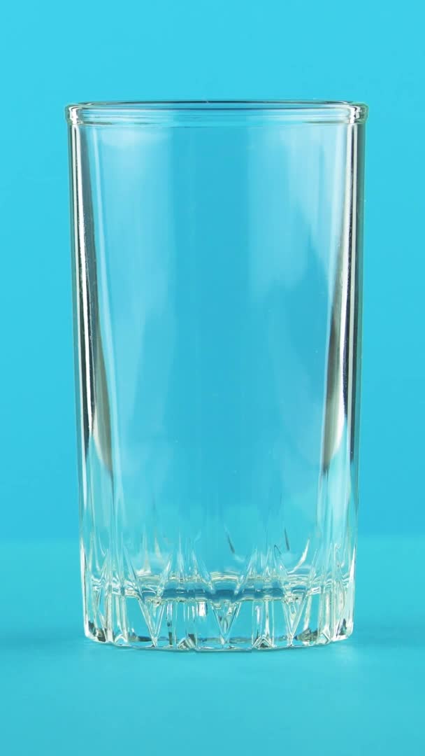 Vídeo vertical 4K close-up de leite bebida fria bebida pooring em vidro roscado fundo azul no estúdio — Vídeo de Stock
