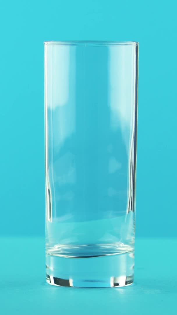 Vertical video 4K close-up shot of yellow lemon fizzy lemonade soda cold beverage drink pooring into glass blue background in studio — Stock Video