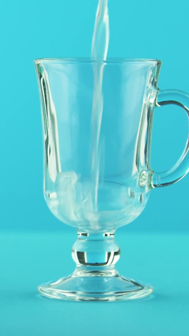 Vertical video 4K close-up shot of yellow lemon fizzy lemonade soda cold beverage drink pooring into latte glass mug blue background in studio — Stock Video