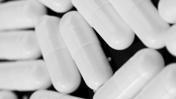 Vertikales Video Weiße Kapseln Antibiotika liegen und rotieren auf schwarzem Hintergrund Nahaufnahme — Stockvideo