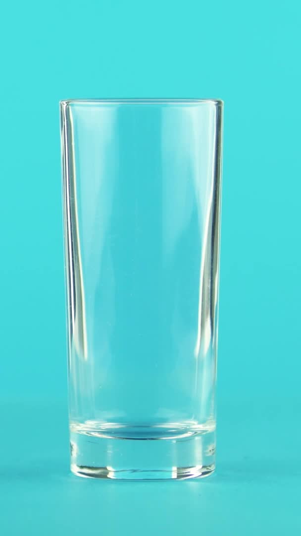 Vertical video 4K close-up shot of fruit fizzy orange cold beverage drink pooring into low glass blue background in studio — Stock Video