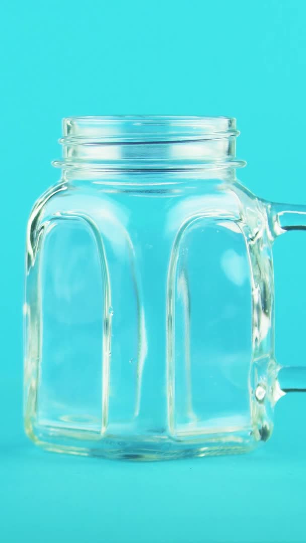 Video verticale 4K close-up shot di frutta succo d'arancia multifrutta bevanda fredda pooring in vaso di vetro tazza sfondo blu in studio — Video Stock
