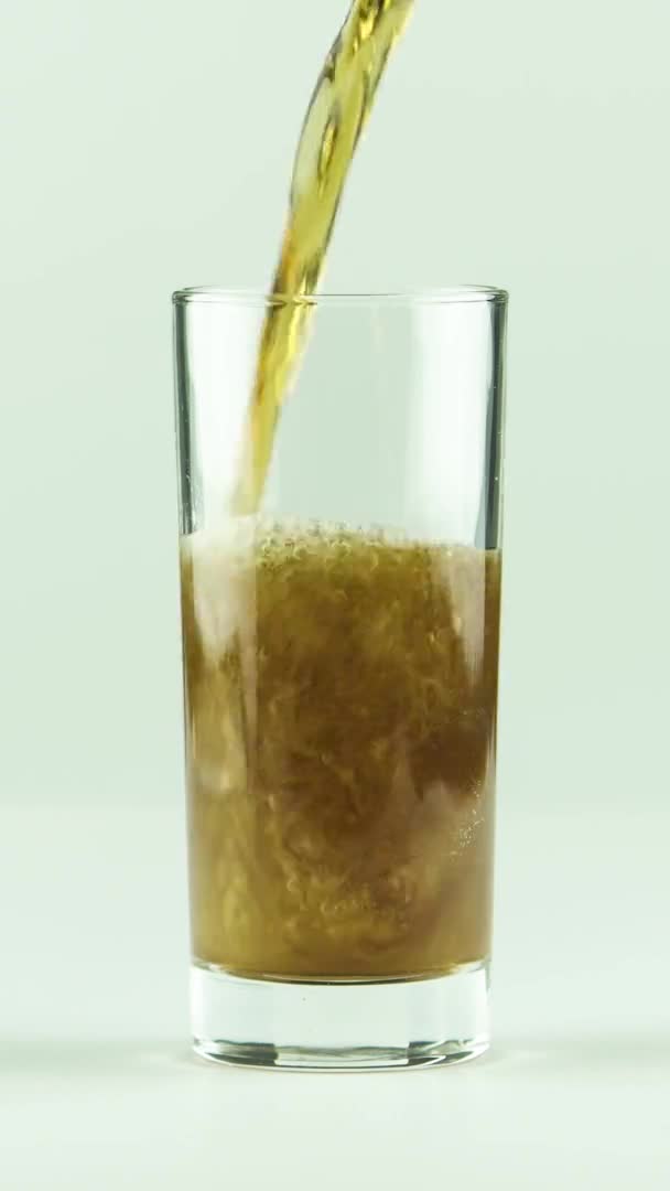 Вертикальное видео Кола выливается в стакан, полный пузырьков и пены изолированы на белом фоне — стоковое видео