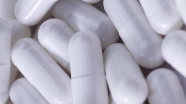 Vidéo verticale De nombreuses capsules d'analgésique blanc reposent sur une table blanche et tournent en gros plan. — Video