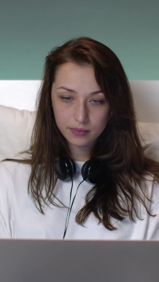 Κάθετη βολή Ελκυστική καυκάσιος γυναίκα με μακριά μαλλιά σε πιτζάμες στο κρεβάτι λειτουργεί σε ένα φορητό υπολογιστή. — Αρχείο Βίντεο