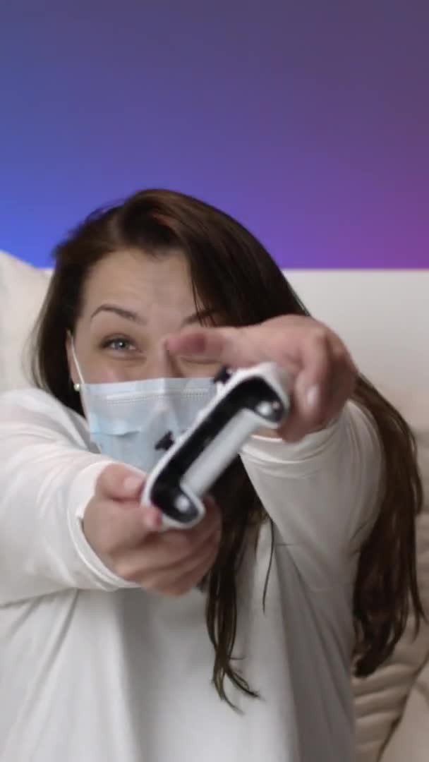 Verticaal schot Aantrekkelijk meisje hebben plezier tijdens quarantaine, speelt spelletjes met joystick thuis — Stockvideo