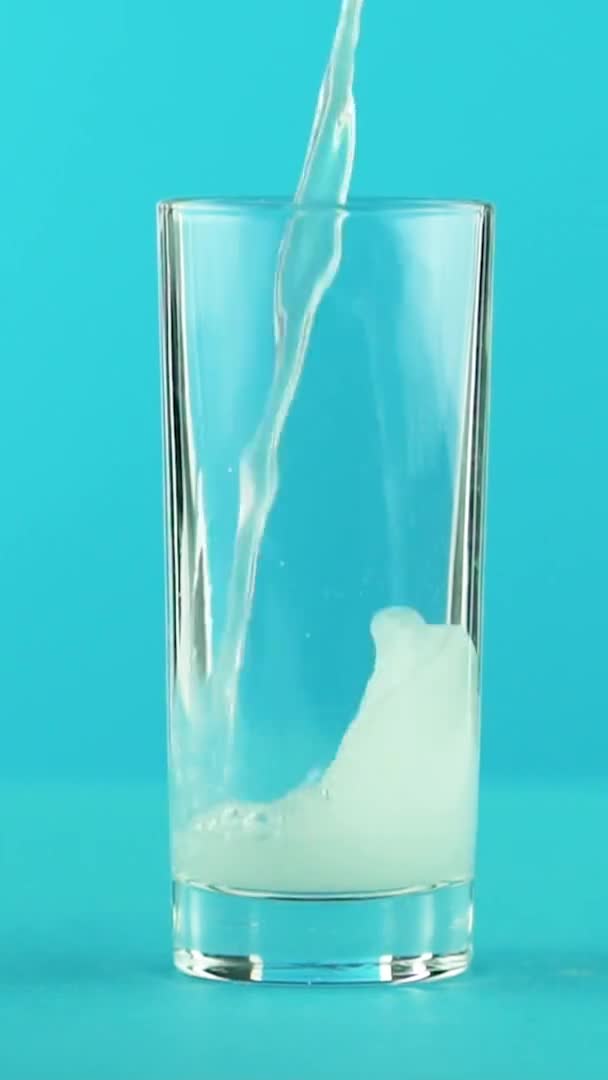Vídeo vertical Slow motion close-up shot of fruit fizzy lemonade soda cold beverage pooring into glass blue background in studio — Vídeo de Stock
