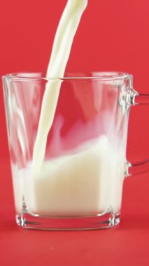 Dikey video yavaş çekim soğuk günlük süt soğuk içecek içecek cam bardak içine poping stüdyo kırmızı arka plan