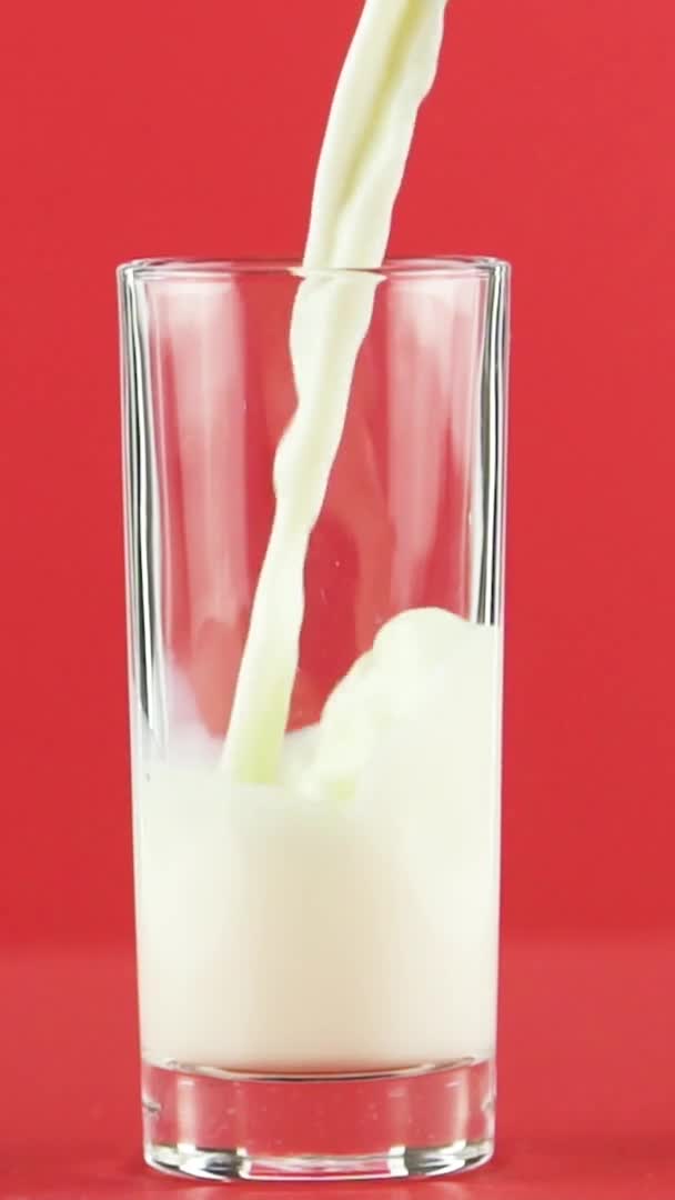 Vídeo vertical Slow motion close-up shot of yellow lemon fizzy lemonade soda cold beverage pooring into glass red background in studio — Vídeo de Stock