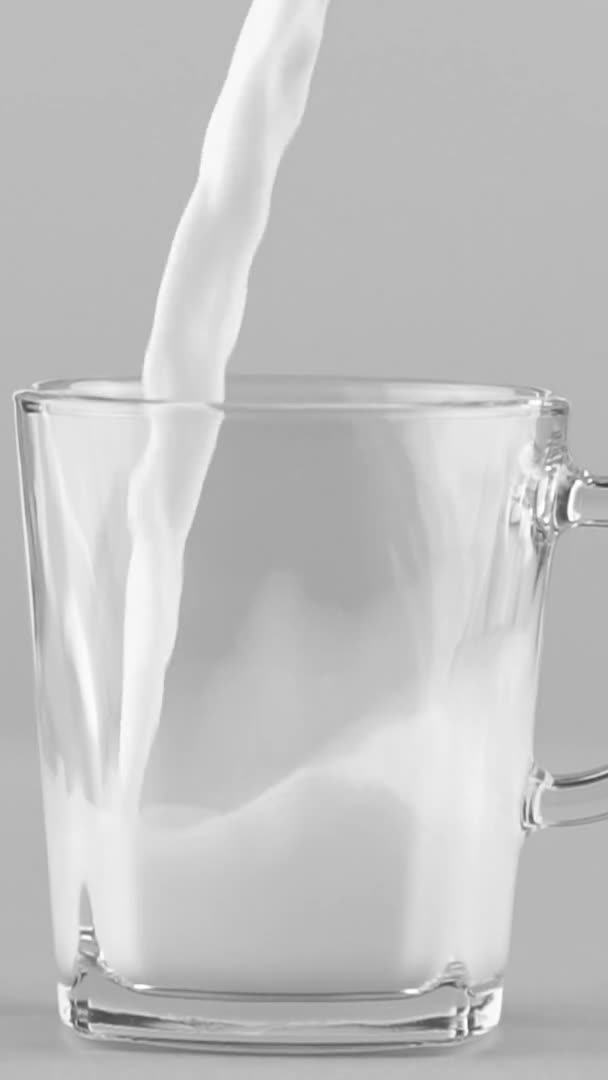 Pionowe wideo Mleko wlewające się do szklanego kubka z bliska odizolowane na jasnoszarym tle — Wideo stockowe