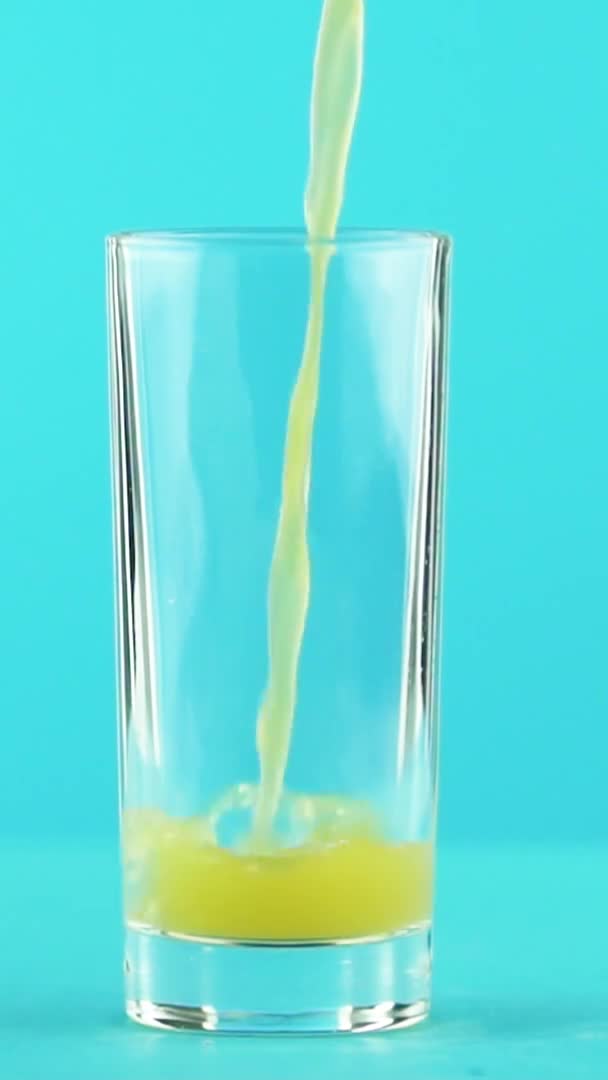 Vídeo vertical Primer plano en cámara lenta de zumo de fruta naranja multifruta bebida fría pooring en fondo azul de vidrio bajo en estudio — Vídeos de Stock