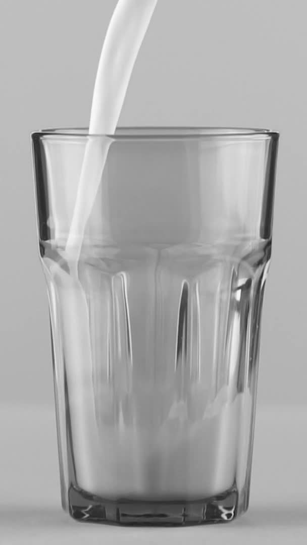 Вертикальное видео Молоко наливается в граненое стекло крупным планом изолировано на светло-сером фоне Медленное движение — стоковое видео