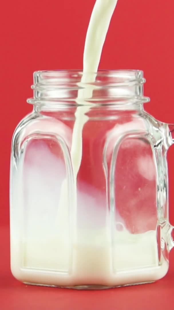 Dikey video yavaş çekim soğuk günlük süt soğuk içecek Stüdyoda cam kavanoz bardak içine sıkışmış içecek kırmızı arka plan — Stok video