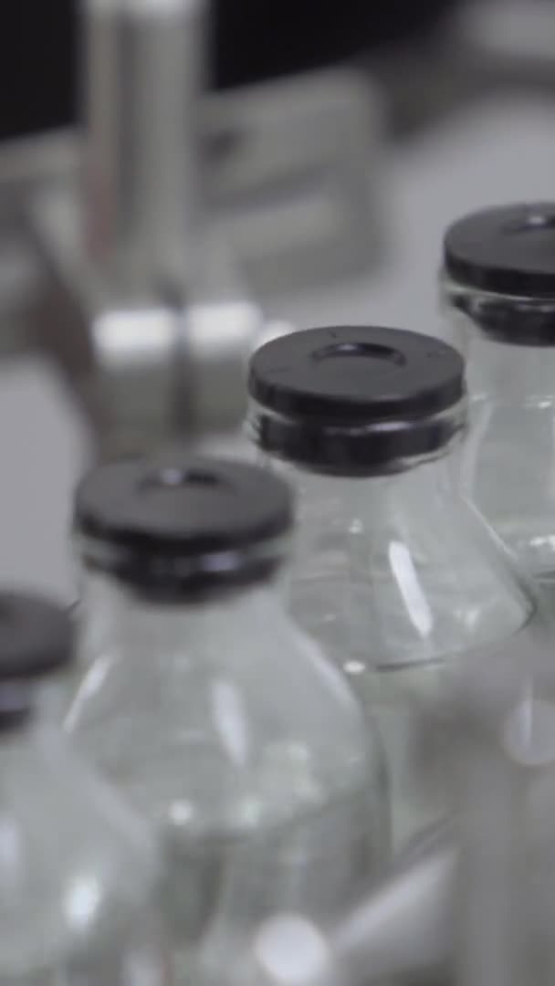 Botellas de vidrio de vídeo verticales llenas y selladas con tapas de goma en una línea de transporte de soluciones médicas enfoque selectivo — Vídeos de Stock
