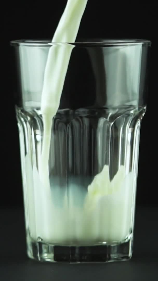 Verticale video Melk gieten in geslepen glas close-up geïsoleerd op zwarte achtergrond Slow motion — Stockvideo