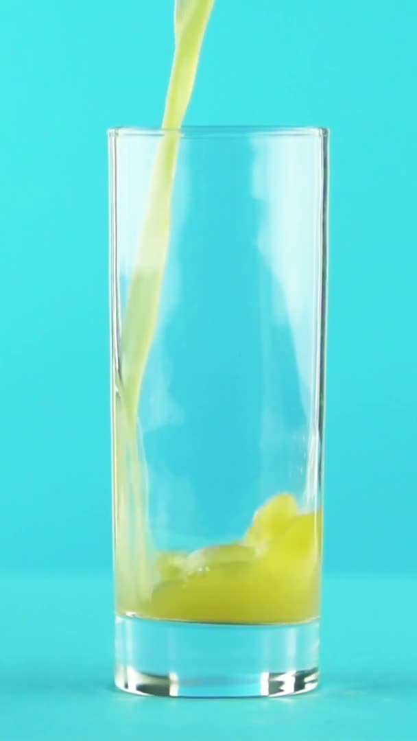 Vídeo vertical Slow motion close-up shot of fruit orange multifruit juice cold beverage pooring into glass blue background in studio — Vídeo de Stock