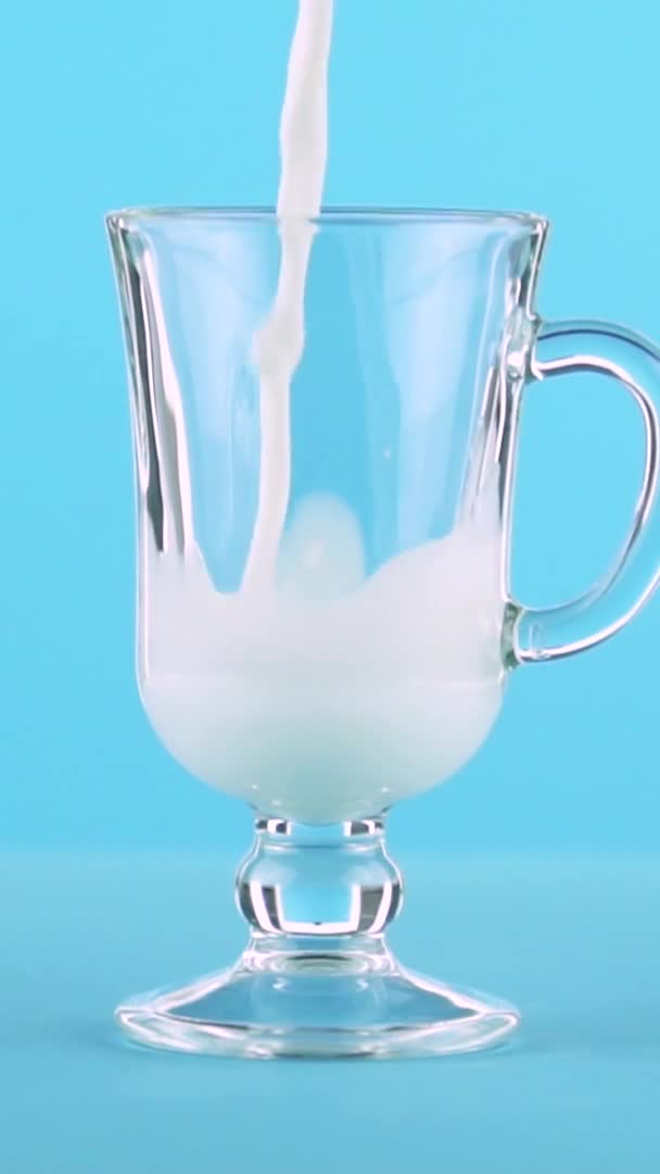 工作室内的垂直视频慢动作特写牛奶冷饮倒入拿铁玻璃杯蓝色背景 — 图库视频影像