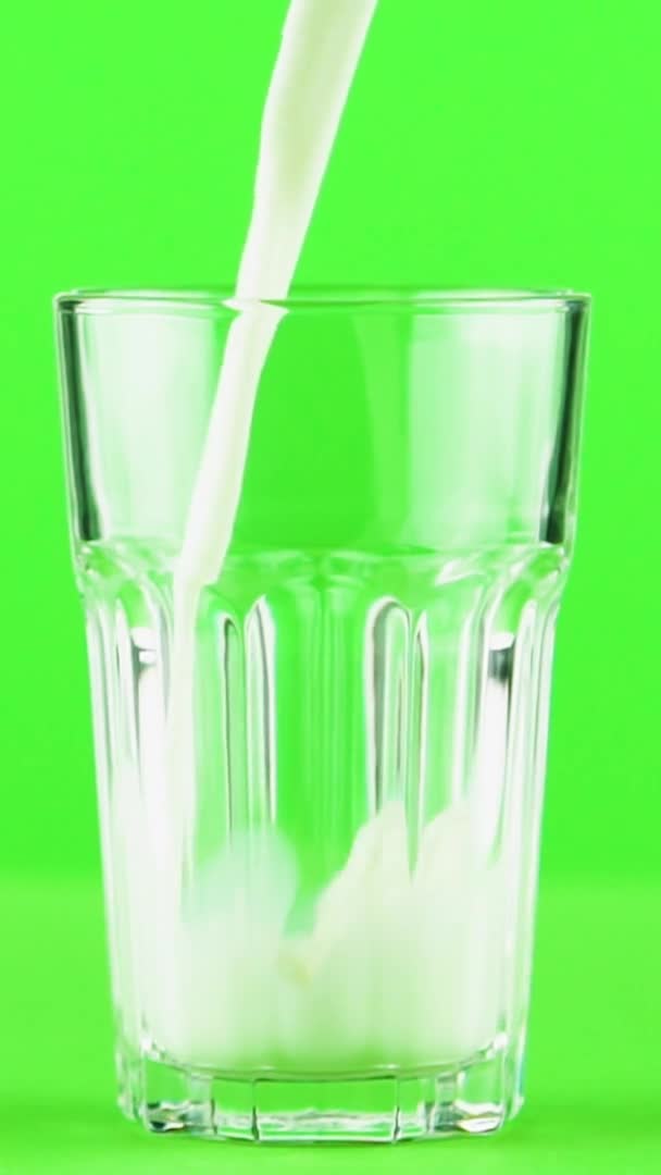 Вертикальное видео Молоко наливается в граненое стекло крупным планом изолировано на светло-зеленом фоне Медленное движение — стоковое видео