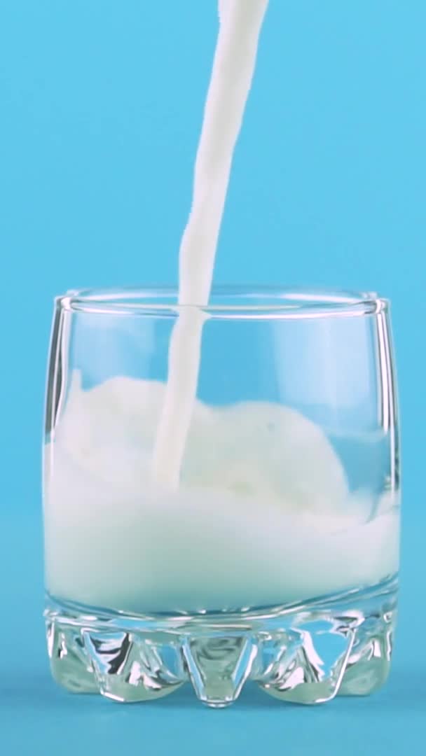 Vídeo vertical Primer plano en cámara lenta de la bebida de leche fría pooring bebida en pequeño hermoso fondo azul de cristal en el estudio — Vídeos de Stock