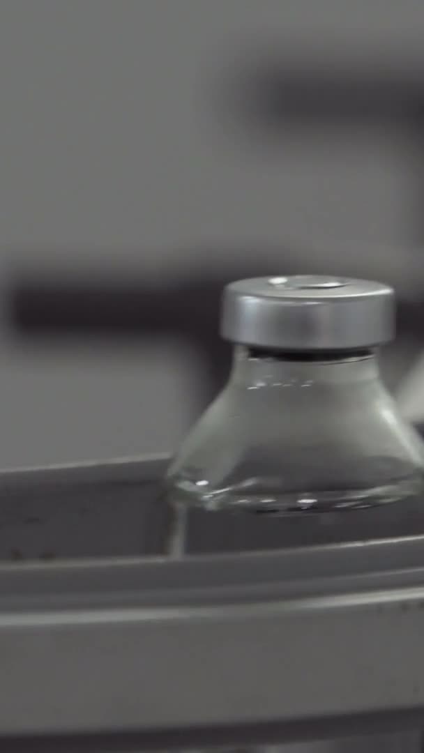 Вертикальное видео стеклянные бутылки заполнены и запечатаны резиновыми и алюминиевыми колпачками на транспортерной линии медицинского решения близко — стоковое видео