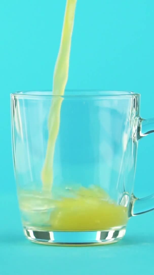 Vertical video Slow motion close-up shot of fruit orange multifruit juice cold beverage drink pooring into glass mug with rounded handle blue background in studio — Stock Video