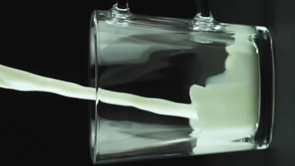 Vídeo vertical Leite derramando em caneca de vidro close-up isolado no fundo preto câmera lenta — Vídeo de Stock
