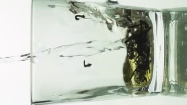 Dikey siyah çay parçacıkları cam şeffaf fincana dökülüyor ve beyaz arka planda izole edilmiş çayı demlemek için kaynar suyla dolduruluyor.