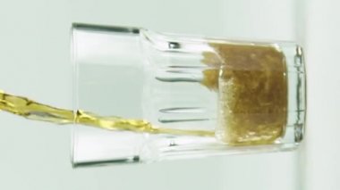 Dikey video Kola, beyaz arka planda izole edilmiş kabarcıklar ve köpüklerle dolu bir bardağa dökülür.