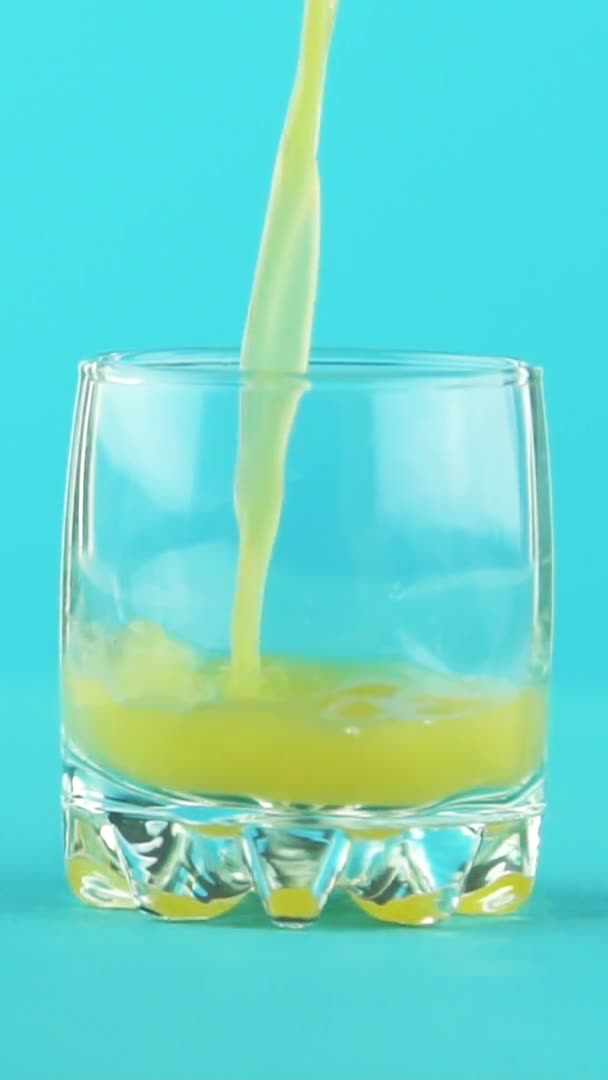 Video verticale Scatto ravvicinato al rallentatore di succo di frutta arancia multifrutta bevanda fredda che si riversa in un piccolo bellissimo sfondo blu vetro in studio — Video Stock