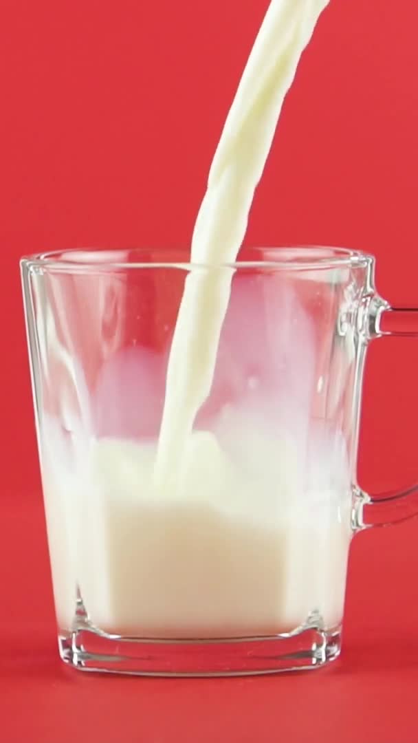 Vertical video Slow motion close-up shot of cold diary milk cold beverage drink pooring into glass mug with handle red background — Stock Video